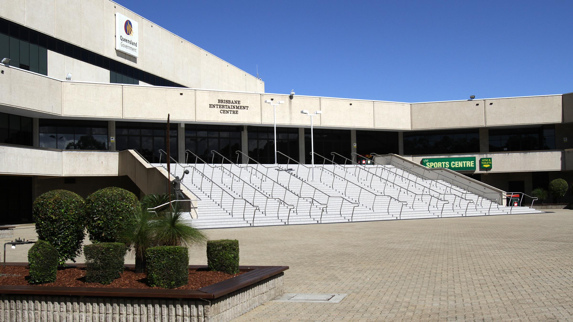 Outside entrance of the Brisbane Entertainment Centre on a sunny day, large flights of stairs lead into the low concrete building