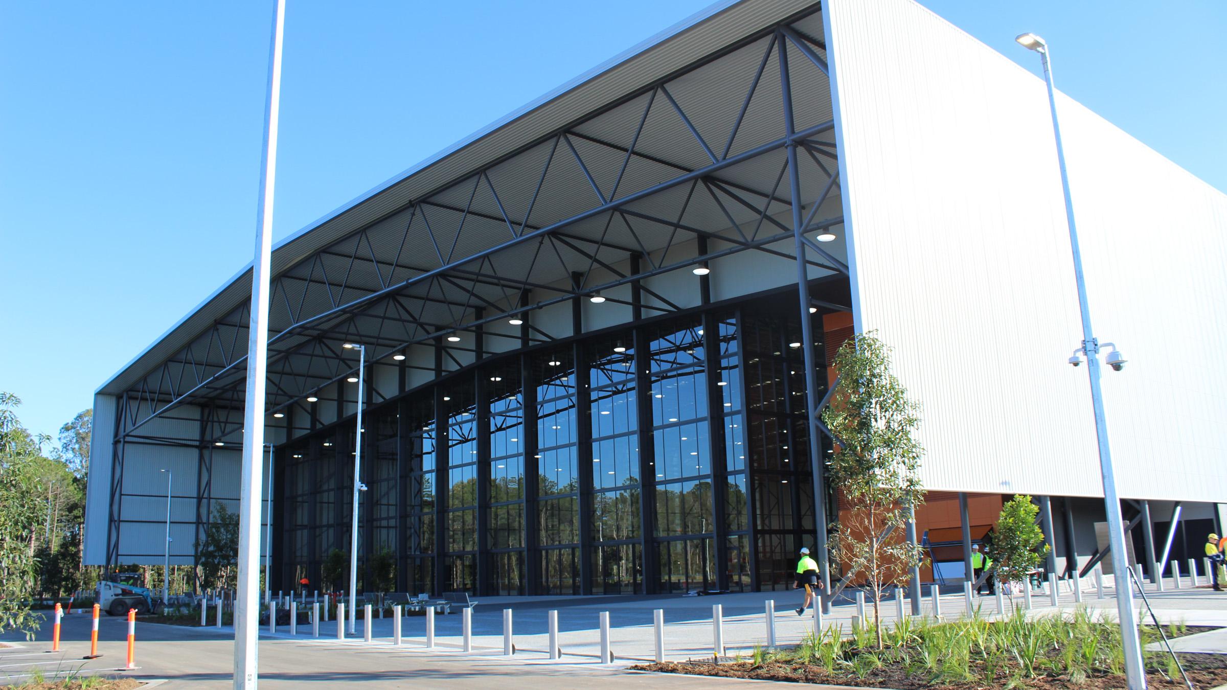 Entrance of the Coomera Indoor Sports Centre on a sunny day, with construction crew walking around