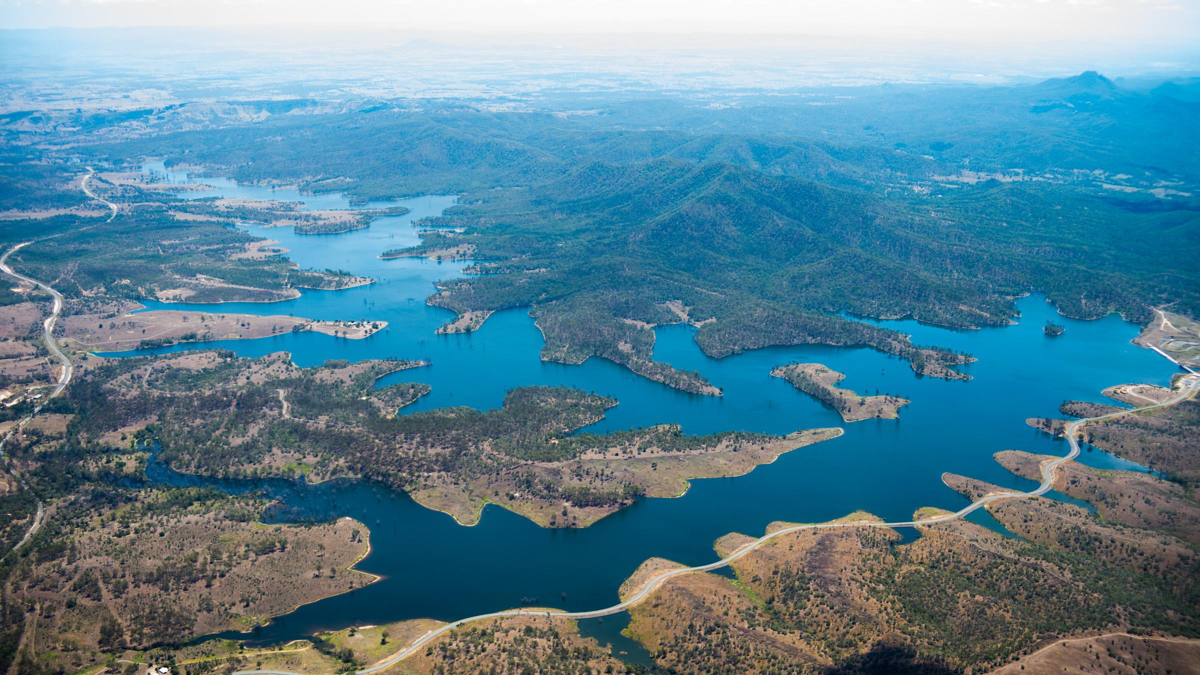 Aerial shot of river near green mountains with a windy road going along the outside of the river