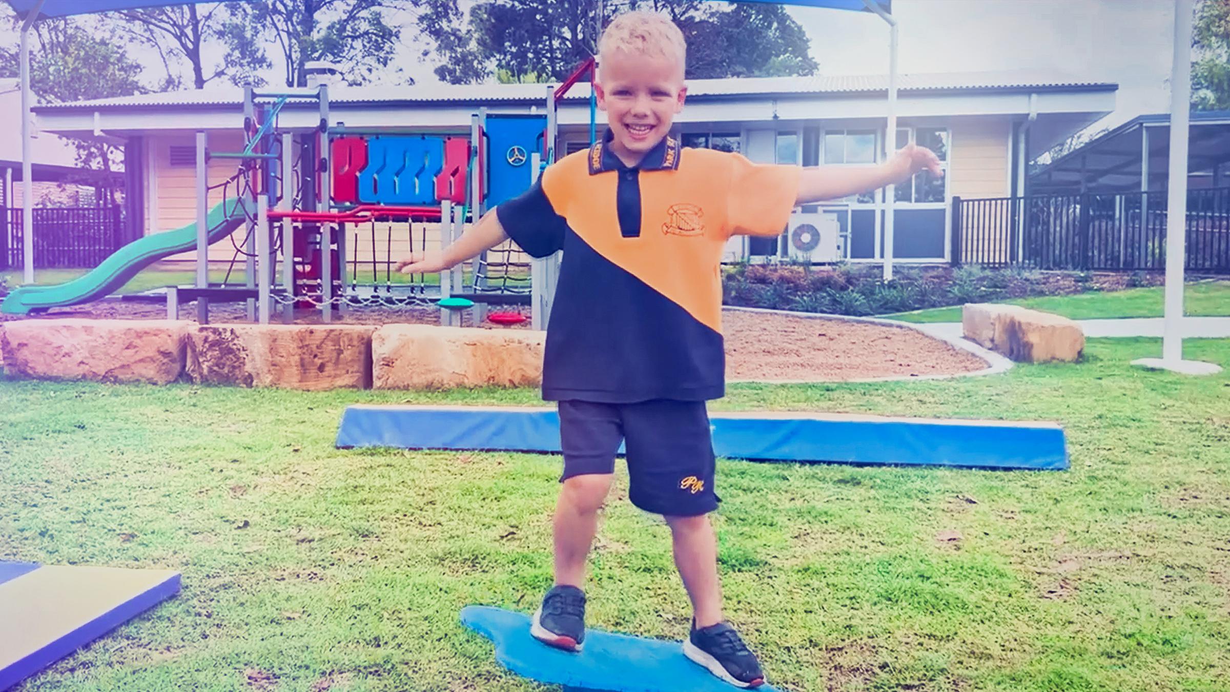 A young boy is standing on equipment in a school playground. 